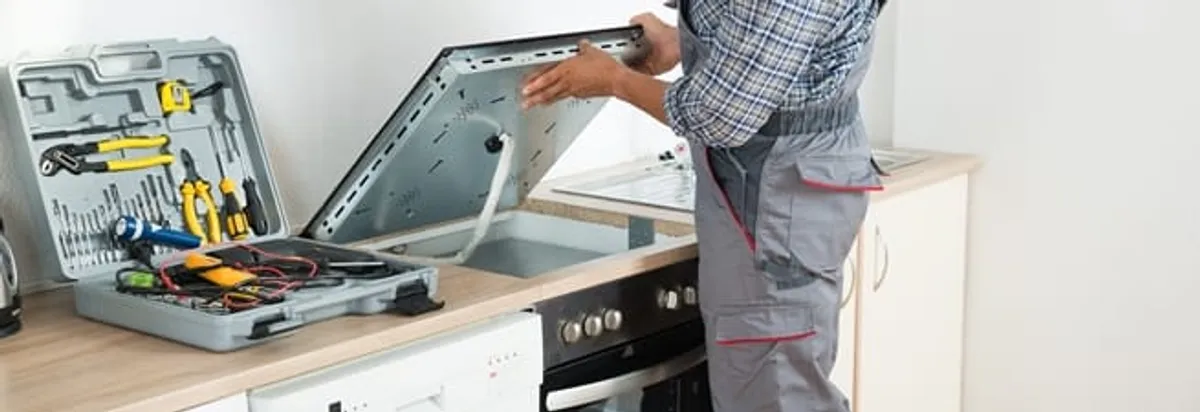 Cooktop repair technician lifting a built-in stovetop for service in Worcester, MA