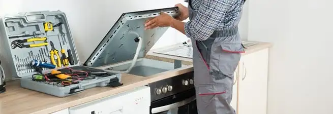 Cooktop repair technician lifting a built-in stovetop for service in Worcester, MA