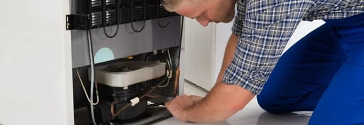 Refrigerator repair technician servicing the compressor and condenser area in Worcester, MA