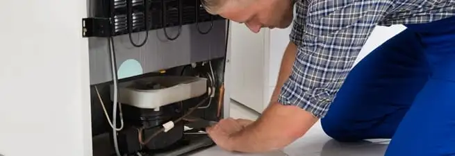 Refrigerator repair technician servicing the compressor and condenser area in Worcester, MA