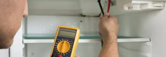 Refrigerator repair technician testing electrical components with a multimeter in Worcester, MA